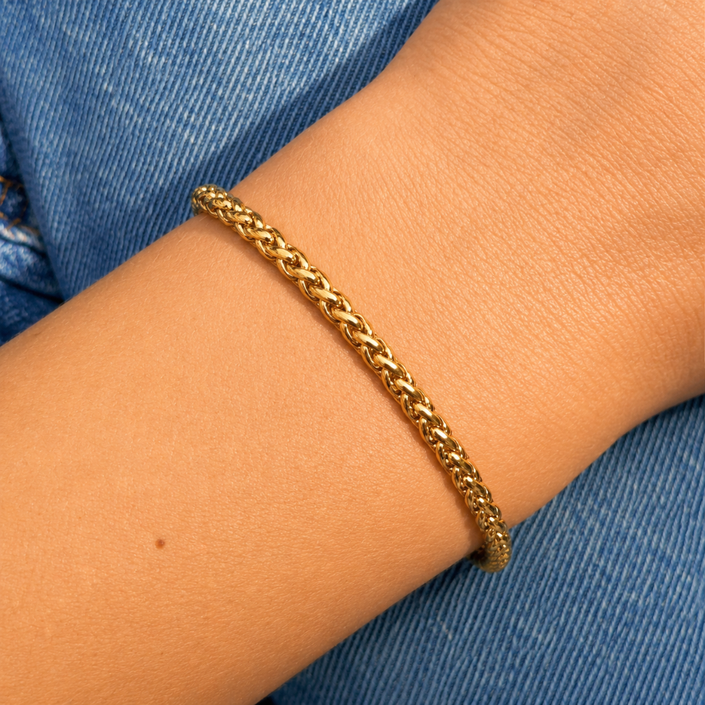 A close-up of a gold chain bracelet worn on a person's wrist, with blue denim fabric visible in the background.