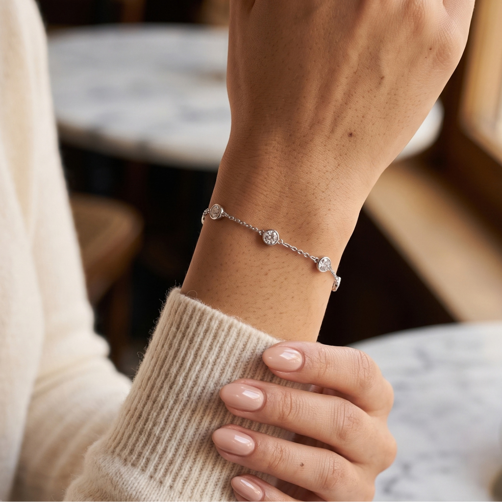 A delicate silver chain bracelet with three small round clear stones worn on a person's wrist, shown in a softly blurred indoor setting.