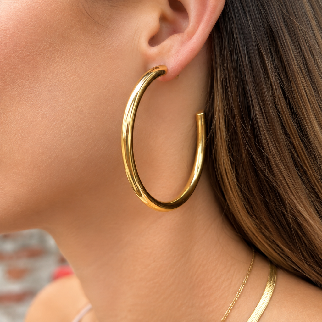 A close-up of a woman's ear wearing a thick, polished gold hoop earring, with her hair and neck visible in the background.