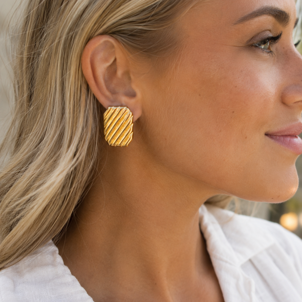 A close-up side profile of a woman wearing a textured gold geometric stud earring with diagonal grooves.