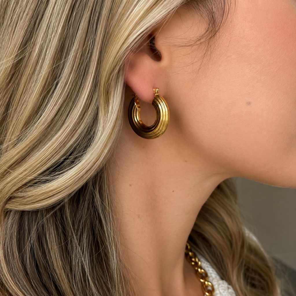 A close-up side profile of a woman wearing a thick, polished gold hoop earring with a textured, ridged outer surface.