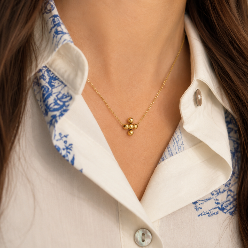 close up of woman wearing gold bead cross necklace on delicate chain with white and blue button down shirt