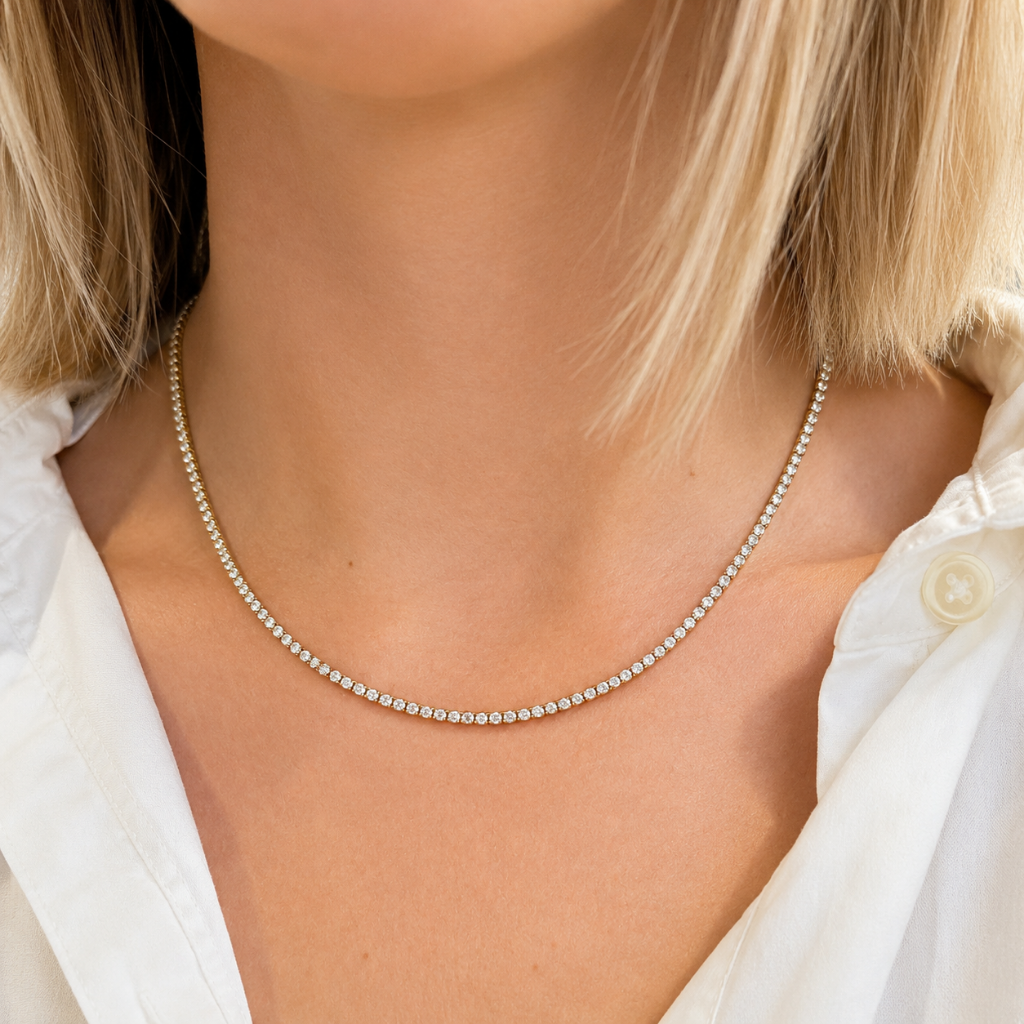 A close-up of a model wearing a delicate silver tennis necklace with small clear stones, styled with a white button-down shirt.