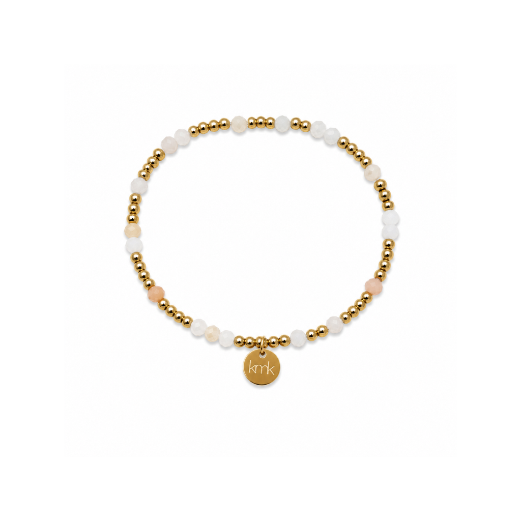 A delicate beaded stretch bracelet featuring white and pale pink stone beads, accented with small gold metallic beads and a round gold initial charm engraved with 'kik'.
