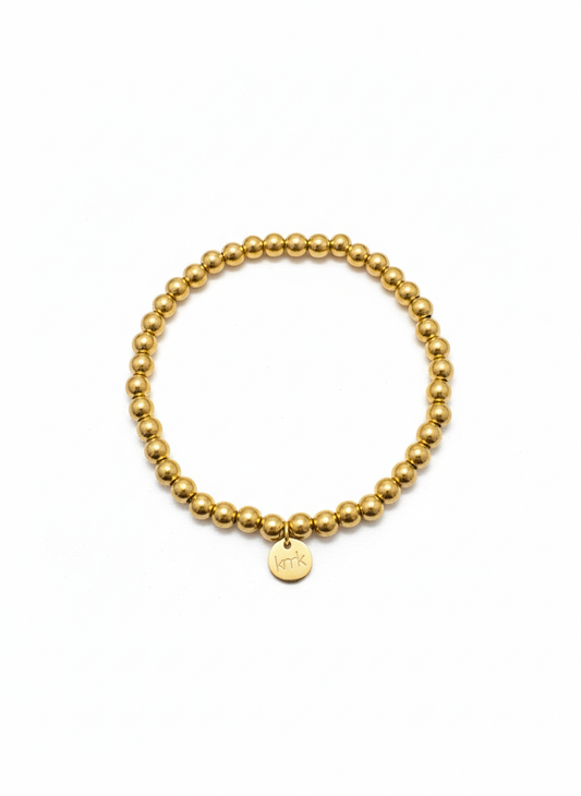Gold beaded bracelet with a round tag on a white background