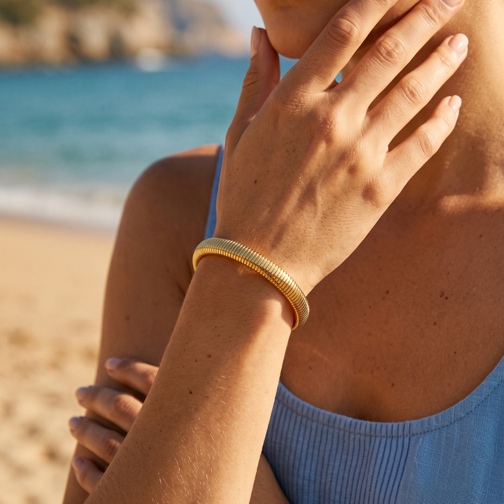 A close-up lifestyle shot of a woman on a beach wearing a textured gold bangle bracelet.