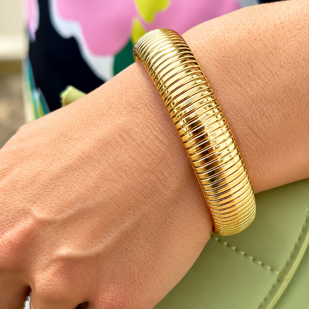 A close-up of a person's wrist wearing a thick, ribbed gold bangle bracelet.