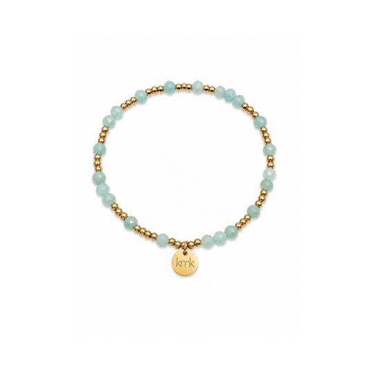 A delicate beaded bracelet featuring light aqua blue-green beads alternating with small gold spacer beads, complete with a gold circular charm engraved with the initials 'k.m'.