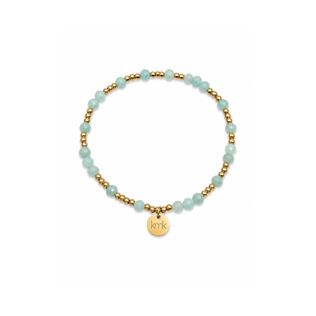 A delicate beaded bracelet featuring light aqua blue-green beads alternating with small gold spacer beads, complete with a gold circular charm engraved with the initials 'KMK'.