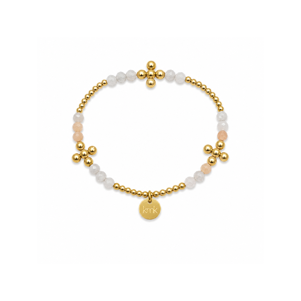 A delicate beaded stretch bracelet featuring gold-plated beads, translucent white beads, pale pink rose quartz beads, and a round gold disc charm engraved with 'RTRK'.