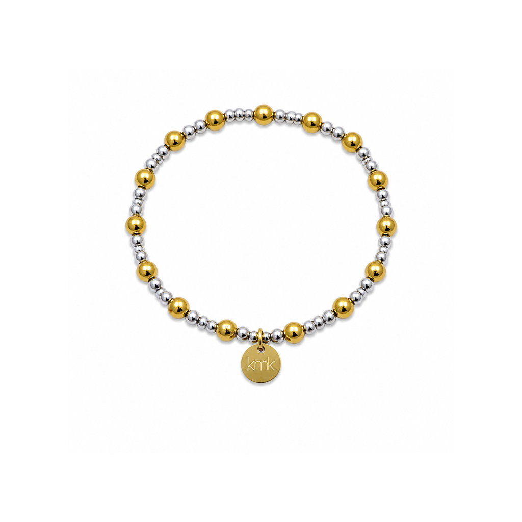 A beaded stretch bracelet featuring alternating polished gold and matte silver metallic beads, with a small round gold disc charm engraved with 'KMK' at the bottom center, shown on a plain white background.