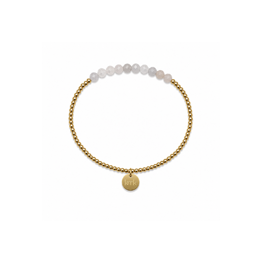 A delicate gold chain bracelet featuring a row of pale, translucent white beads at the top and a small round gold disc charm engraved with initials, set against a plain white background.