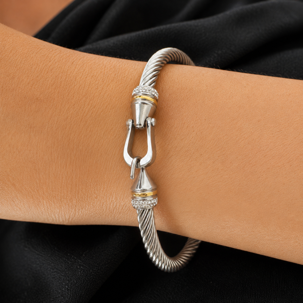 A silver-toned twisted cable bangle bracelet with gold accents and a clasp, shown worn on a person's wrist against a black fabric background.