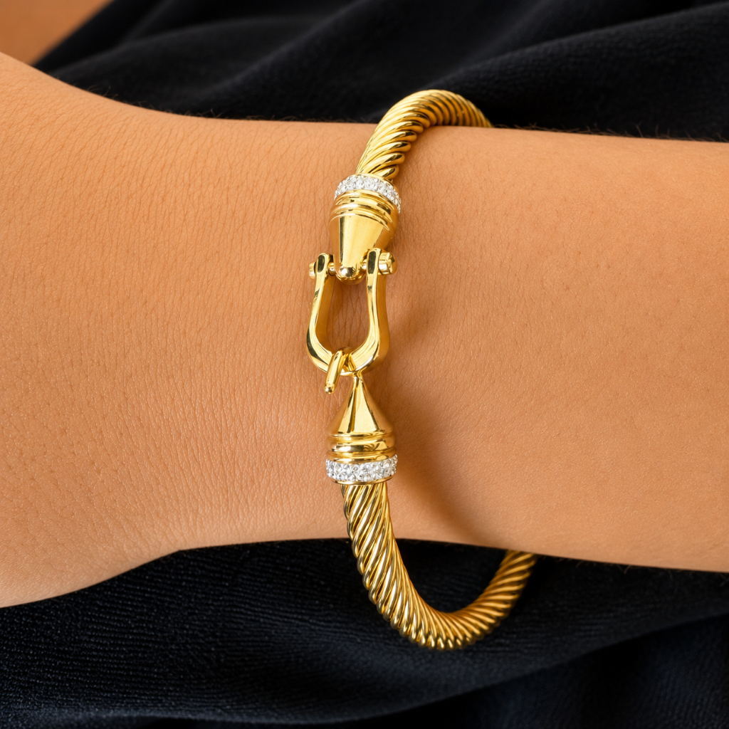 A gold-toned twisted rope bangle bracelet with diamond accents on the clasp, shown worn on a person's wrist against a black fabric background.