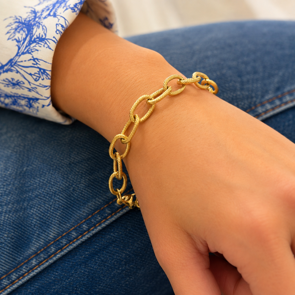 gold textured link bracelet on wrist with model wearing blue jeans and a white and blue floral top 