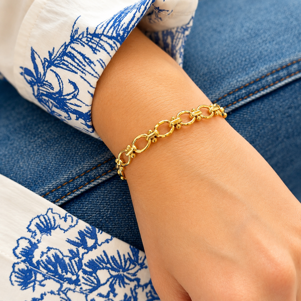 gold chain bracelet on model's wrist wearing blue jeans and white and blue floral printed top 