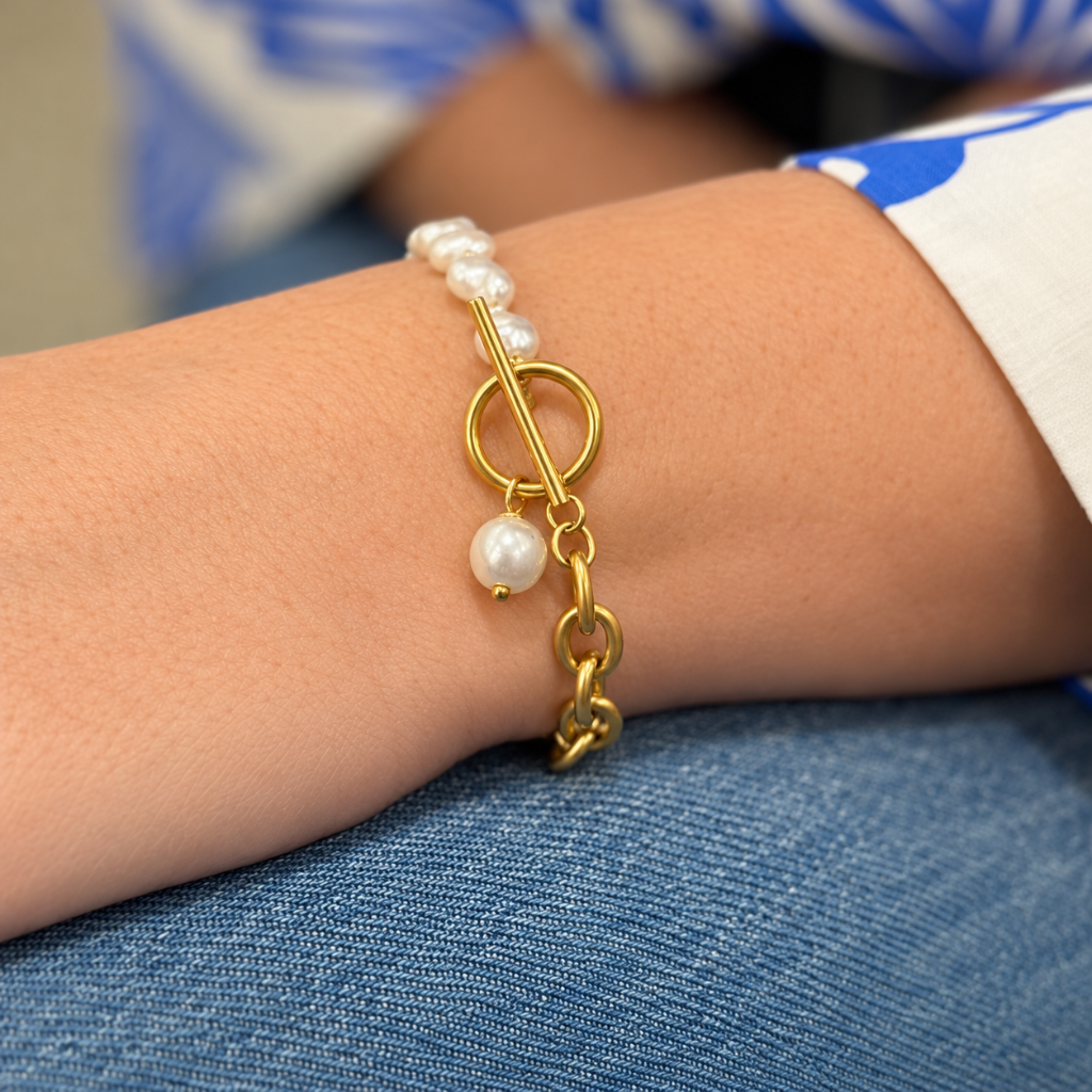 A gold toggle bracelet with white pearl beads and a dangling pearl charm, shown worn on a person's wrist.