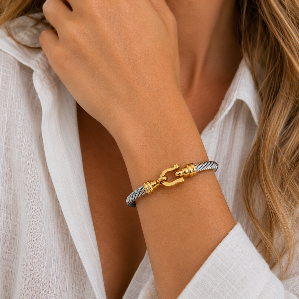A close-up of a person's wrist wearing a silver and gold cable-wrapped bracelet with a gold anchor clasp, paired with a white linen shirt.