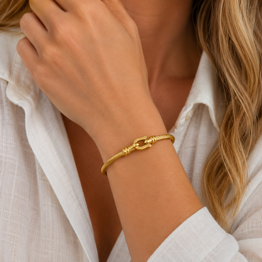 A close-up of a woman's wrist wearing a gold chain bracelet with a decorative clasp, paired with a white collared shirt.