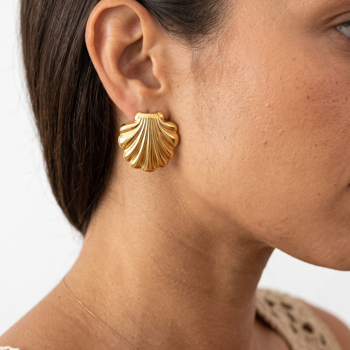 A close-up of a model's ear wearing a textured, ribbed gold shell-shaped stud earring against a clean white background.
