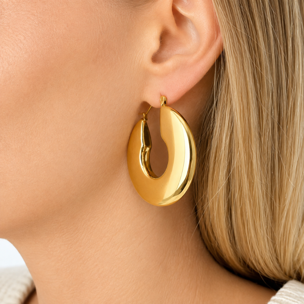 A close-up of a woman's ear wearing a polished, chunky gold crescent-shaped hoop earring.