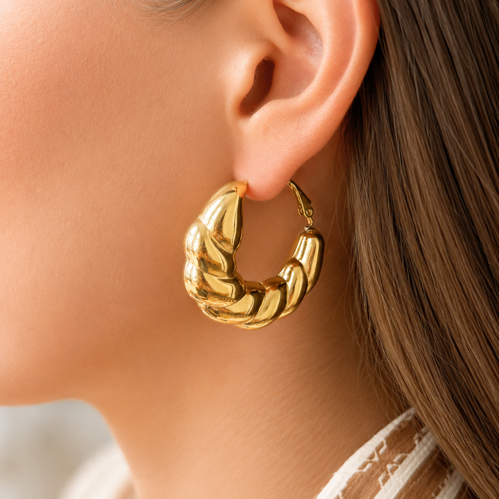 A close-up of a model's ear wearing a chunky, twisted gold hoop earring.
