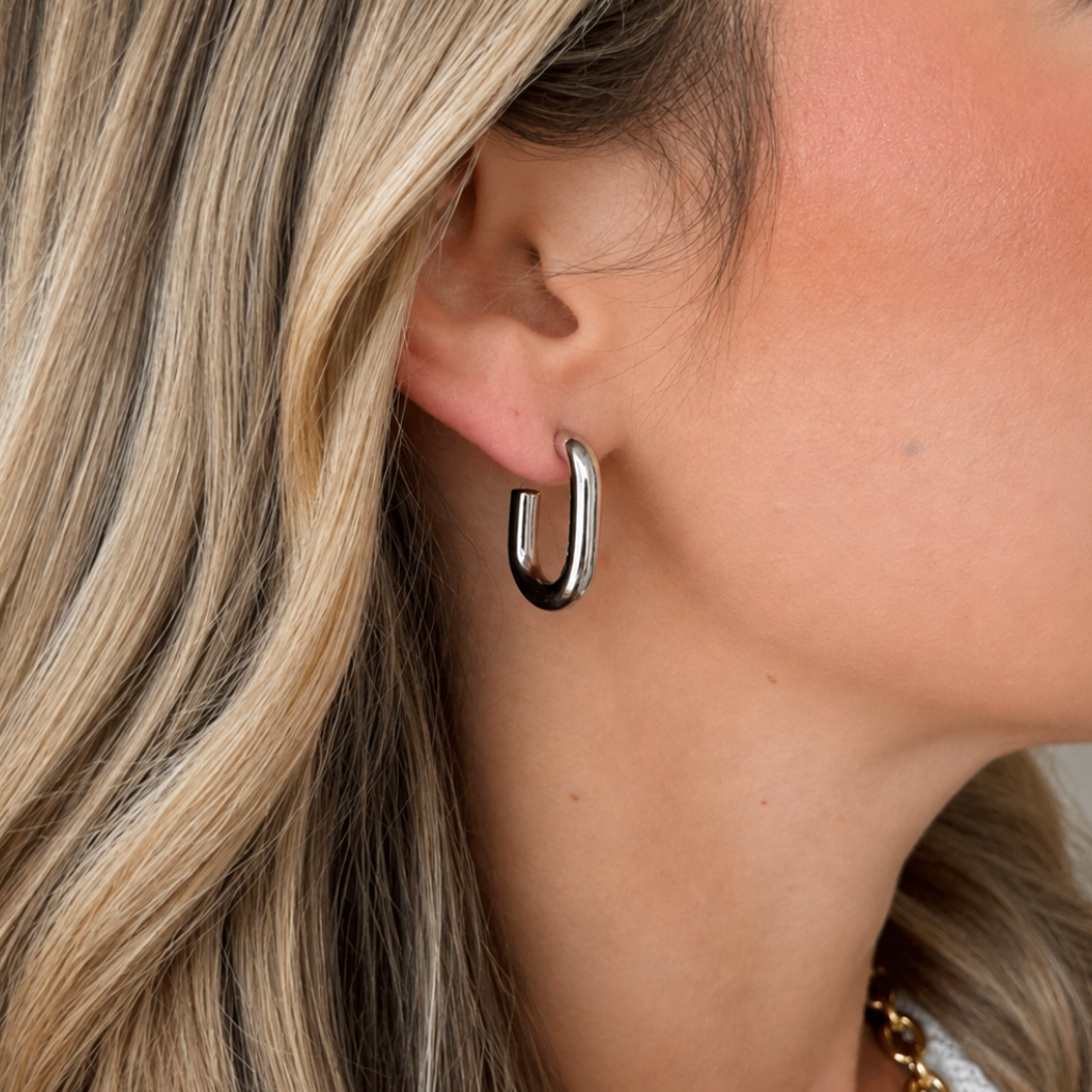 A close-up of a woman's ear wearing a polished silver U-shaped hoop earring.