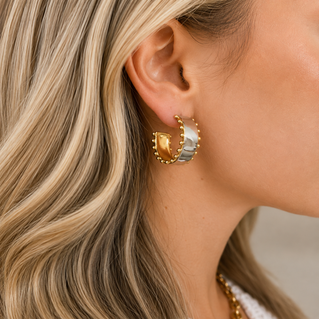 A close-up of a woman's ear wearing a two-tone gold and silver crescent-shaped hoop earring with beaded edges.