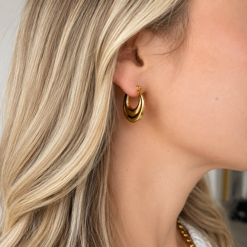 A close-up of a woman's ear wearing a polished gold triple-hoop earring, with her blonde hair and skin visible.