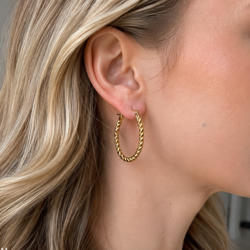 A close-up of a woman's ear wearing a small gold hoop earring with a twisted rope texture.