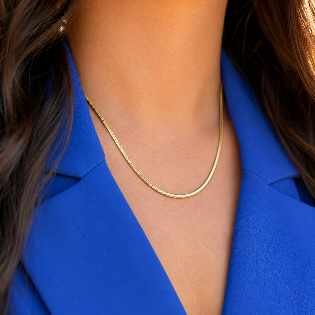 A close-up of a delicate gold chain necklace worn by a person in a bright blue blazer.