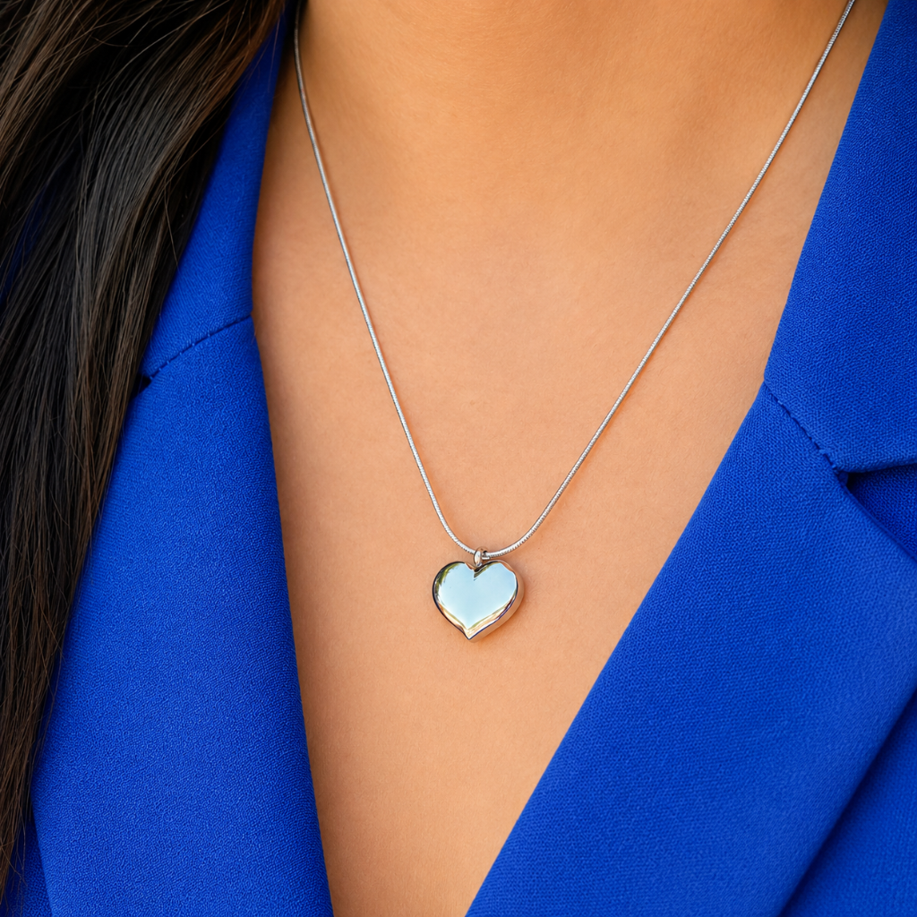 A close-up of a person wearing a silver heart pendant necklace with a light blue inlay, styled with a bright blue blazer.