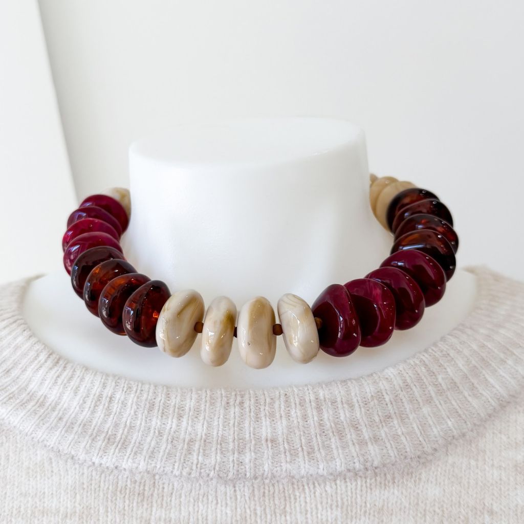 A chunky beaded necklace made of alternating deep burgundy-red translucent beads and smooth cream-colored beads, displayed on a white mannequin bust wearing a cream knit sweater.