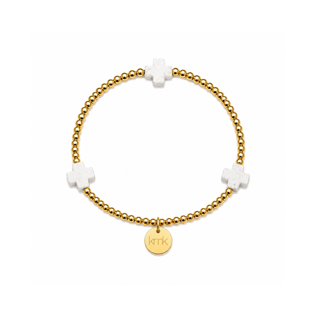 A gold beaded bracelet with three white cross charms and a round gold disc charm engraved with 'kkr', shown on a plain white background.