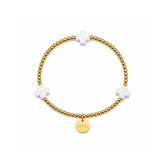 A gold beaded bracelet with three white cross charms and a round gold disc charm engraved with 'kkr', shown on a plain white background.