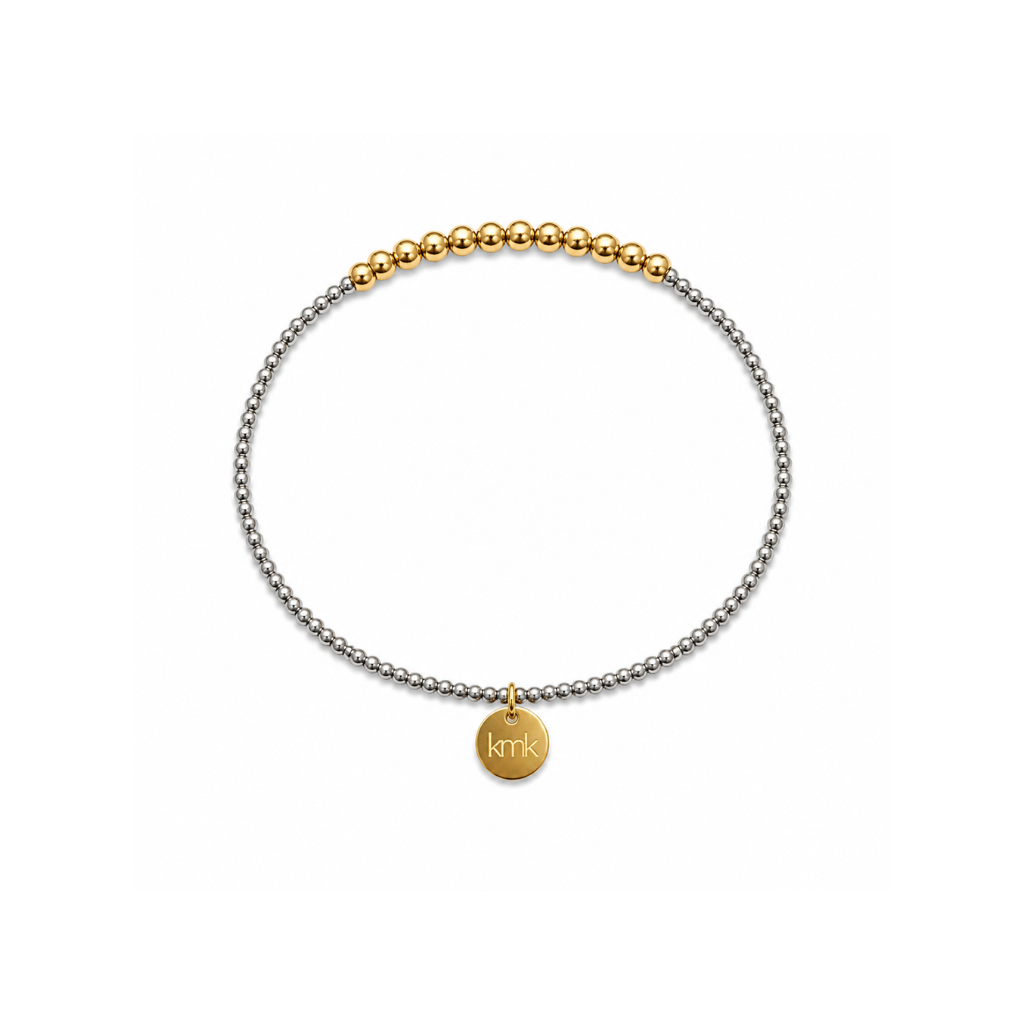 A delicate two-tone beaded bracelet with a silver-toned chain, a gold-toned beaded section at the top, and a small round gold disc charm engraved with 'kmk', shown on a plain white background.