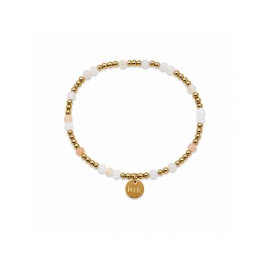 A delicate beaded stretch bracelet featuring white and pale pink stone beads, accented with small gold metallic beads and a round gold initial charm engraved with 'kik'.