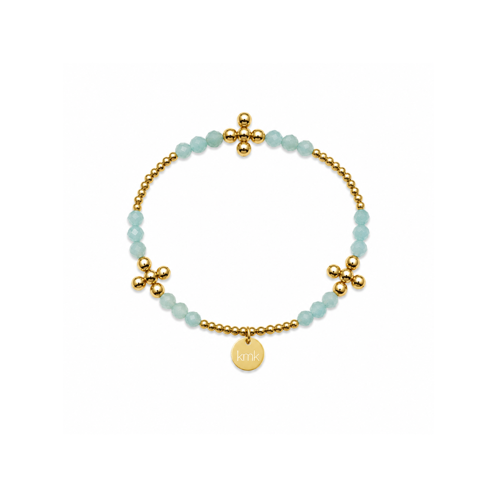 A delicate gold beaded bracelet with light blue faceted beads, gold flower-shaped charms, and a small round gold disc charm engraved with 'KMK', displayed on a clean white background.
