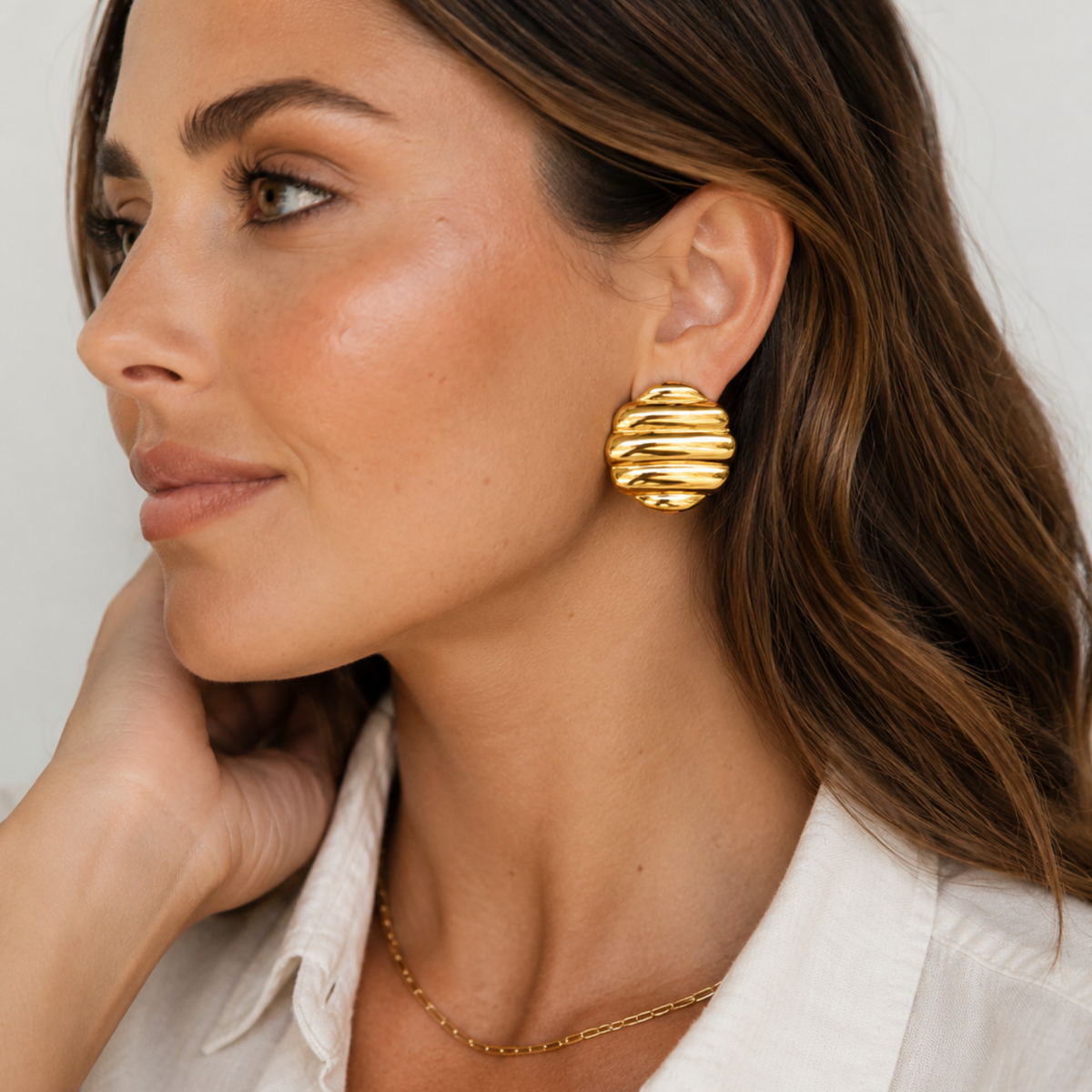 close up of woman wearing gold circle stud earring with white background and white button down shirt 